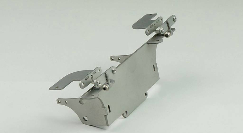 A metal component with multiple hinges and moving parts, likely a mechanical carrier or mounting bracket.