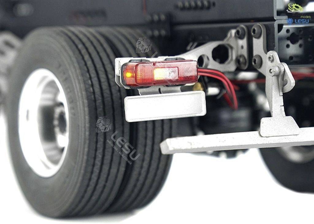 'Lorry rear light with red and white lenses, mounted on a metallic frame in front of a large tyre.'