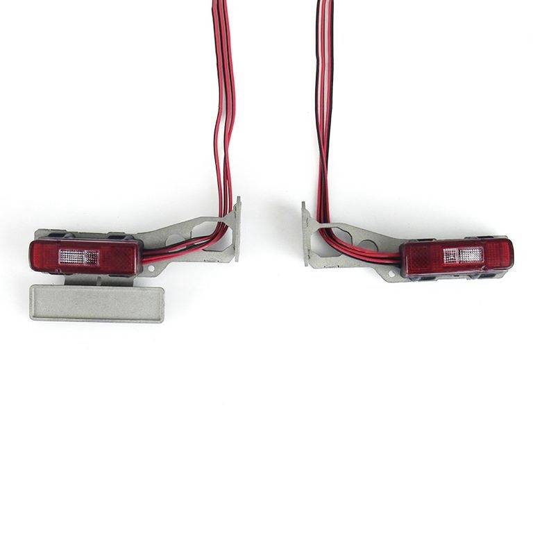Two red car tail lights with cables, on a white background. They are disconnected and show internal electrical components.