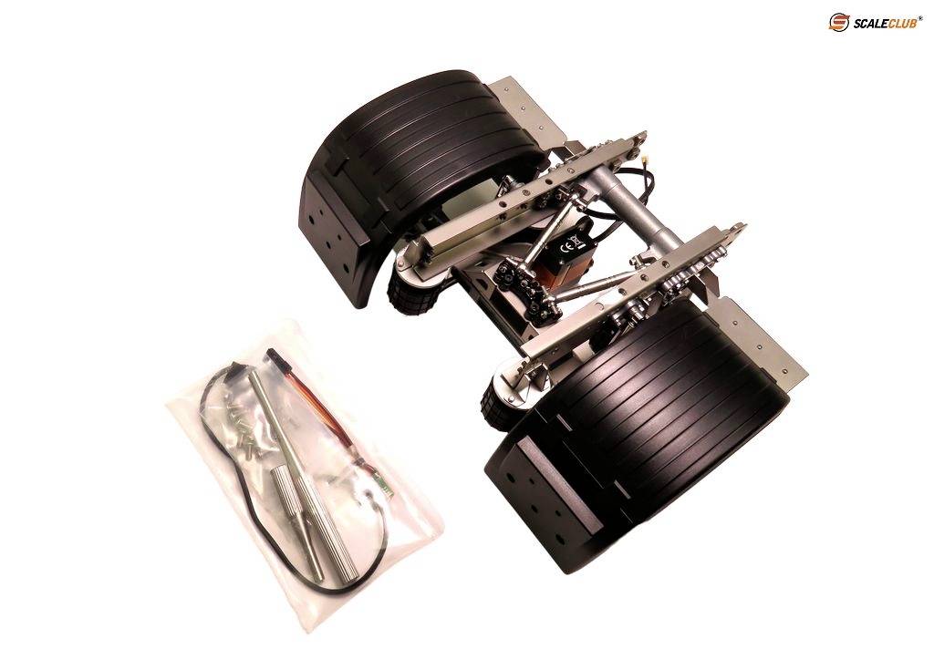 Parts of an RC lorry kit, including a chassis with two large black wheels and a small bag of accessories positioned to the right.