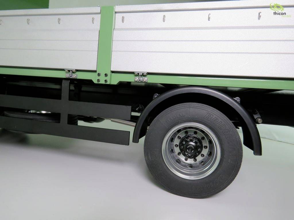 A partial section of a green lorry with a metal loading bed. A wheel and part of the vehicle bodywork are visible.