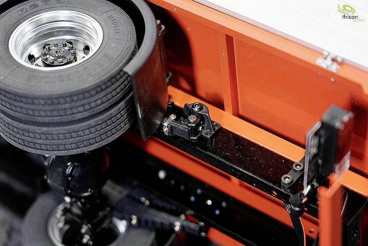 Close-up of an orange chassis with a spare tyre and camera unit, likely for technical or testing purposes. A logo is positioned in the top right corner.