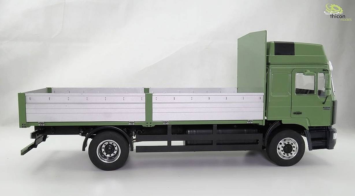 A green lorry without cargo is parked sideways.