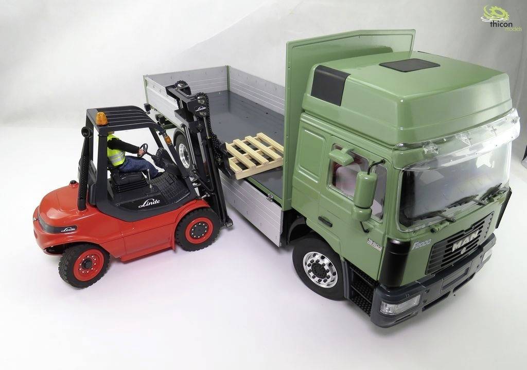 A forklift truck lifts a wooden pallet onto the loading area of a green lorry. A driver is operating the red forklift truck.