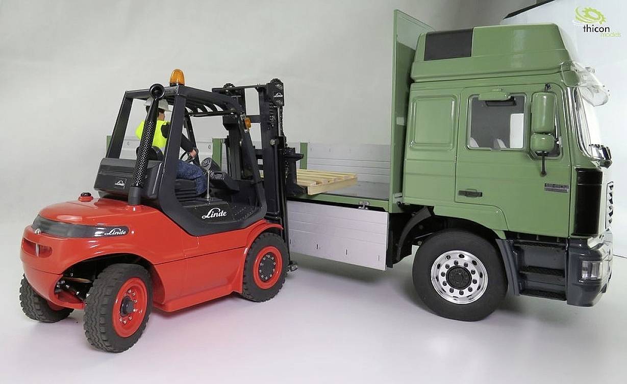 A red forklift is loading wooden pallets onto the loading bay of a green lorry. One person is operating the forklift.