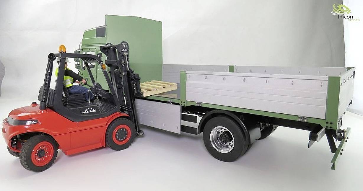 A red forklift truck lifts a pallet onto the loading area of a green lorry. The driver sits attentively in the forklift.