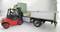 A red forklift truck lifts a pallet onto the loading area of a green lorry. The driver sits attentively in the forklift.