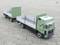 A green model lorry with a trailer is parked on a paved surface. The trailer is open and empty.