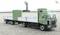 Green lorry with trailer parked on a paved area, white wall with climbing plant in the background; no people visible.