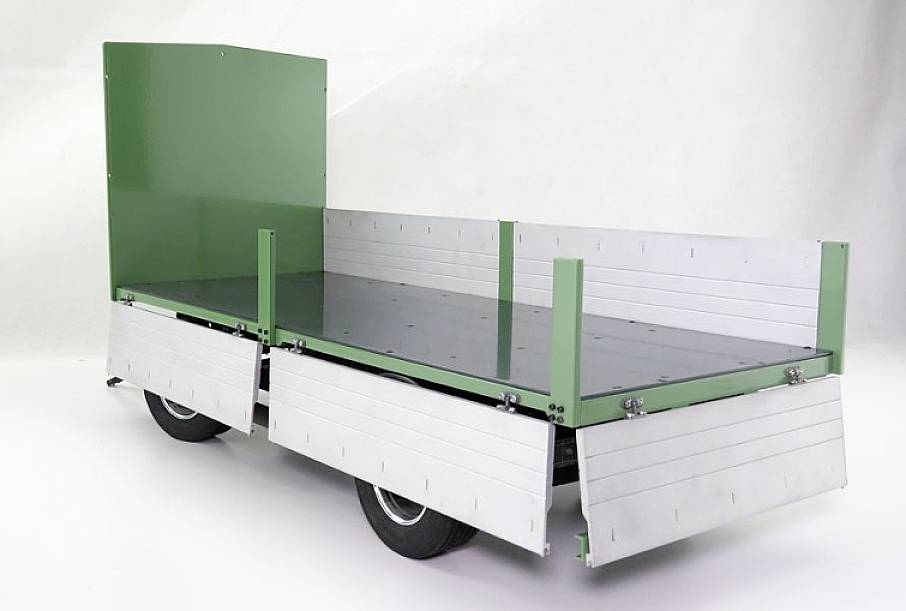 Green trailer with metal side walls mounted on wheels, positioned against a white background, suitable for transporting goods or materials.