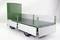 Green trailer with metal side walls mounted on wheels, positioned against a white background, suitable for transporting goods or materials.