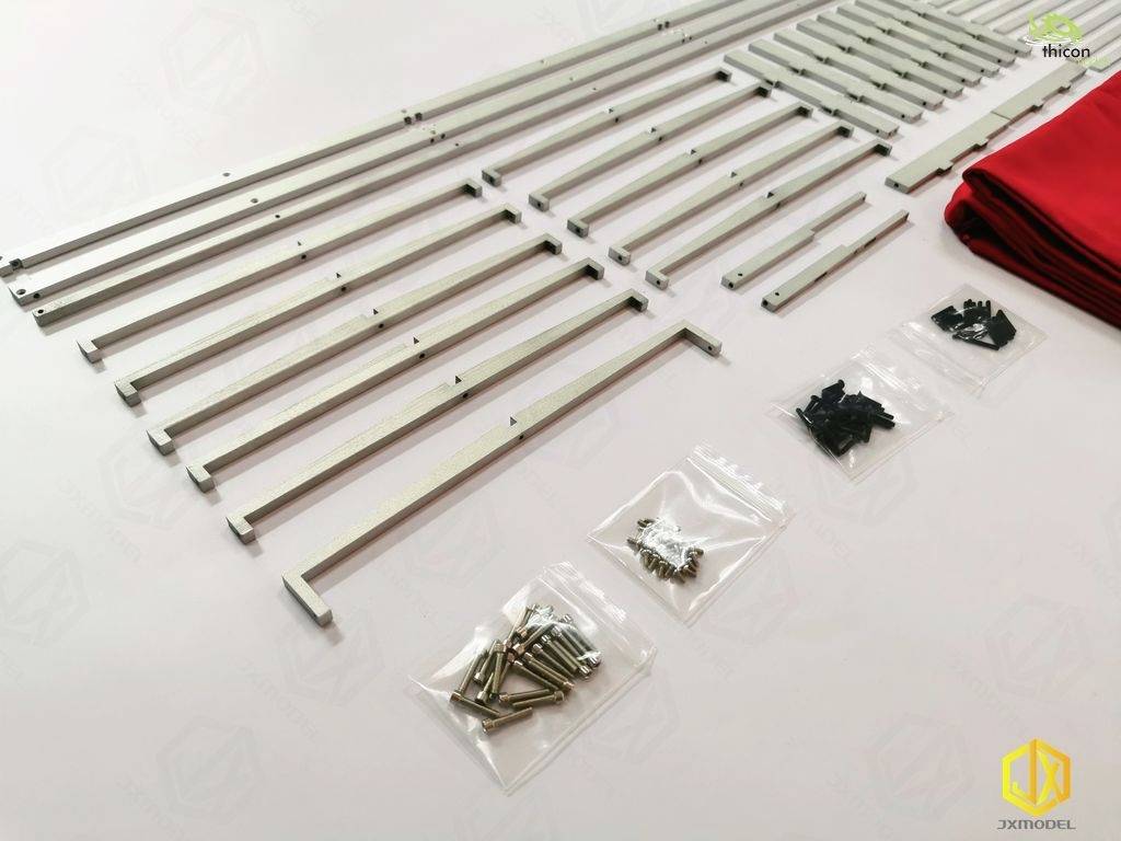 Components of a model kit, including metal rods, screws, and red fabric pieces, arranged neatly on a white surface.