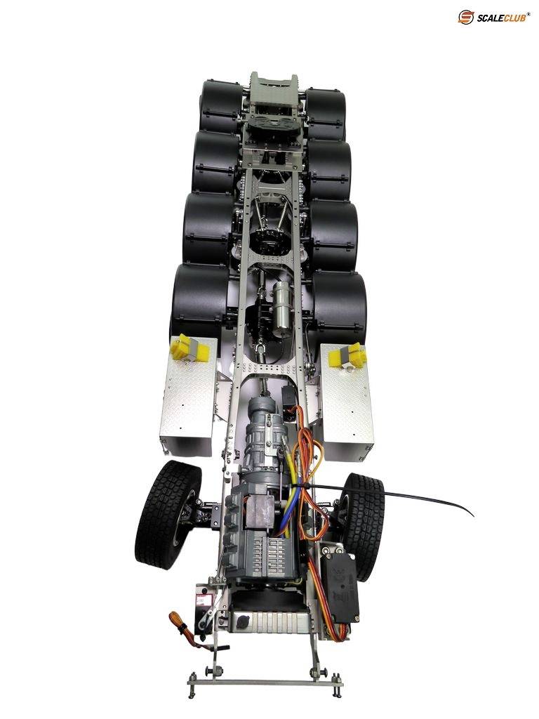 Long model truck chassis without bodywork, with visible electronics, wheels, and cylinders. Top view.