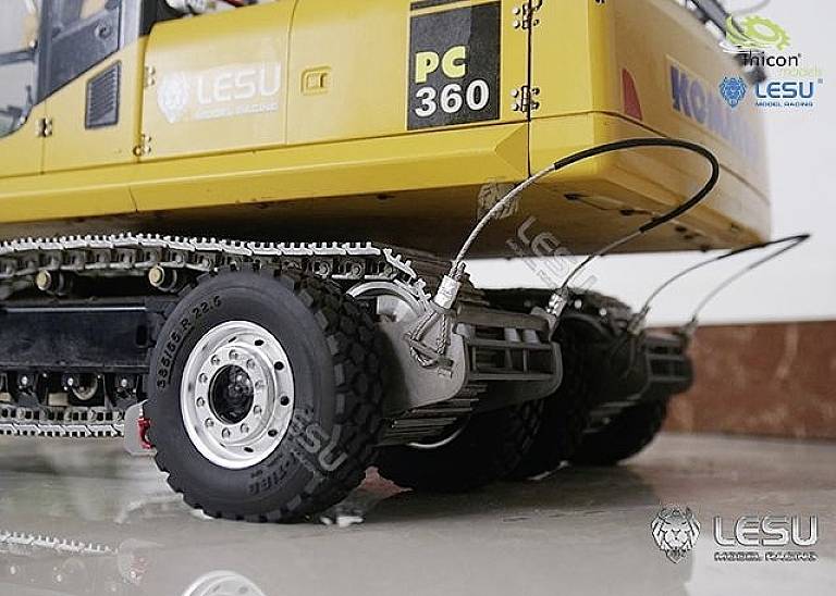 Yellow excavator with rubber tyres and metal tracks, showing a close-up of the rear wheels and track mechanism, in front of a marble wall.
