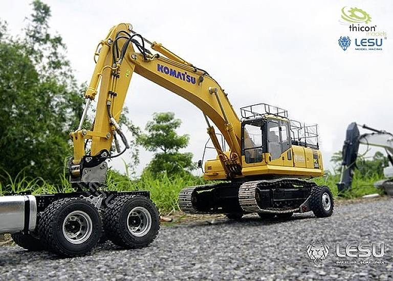 A yellow excavator is lifting a vehicle on a road. Trees and another excavator can be seen in the background.
