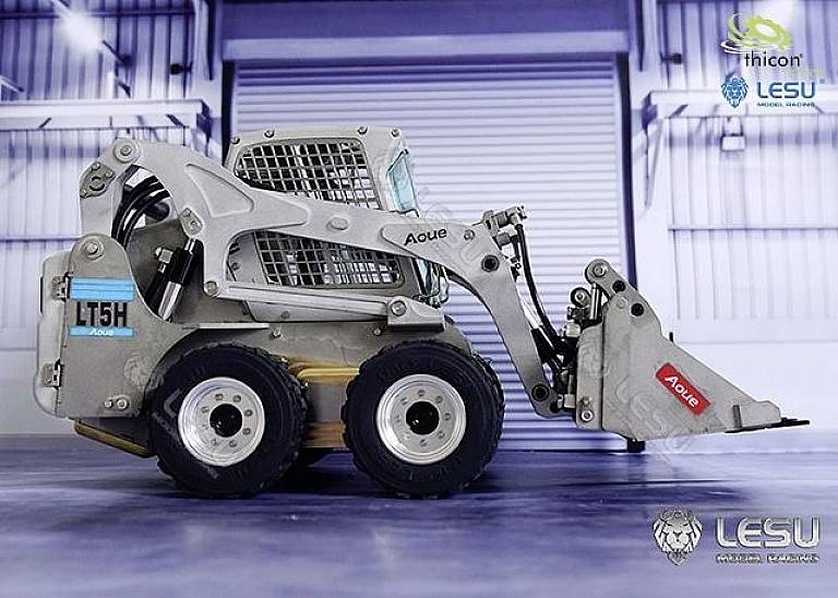 A mini loader with the markings 'Aoue' and 'LT5H' stands in an industrial space. It has four wheels and a small bucket.