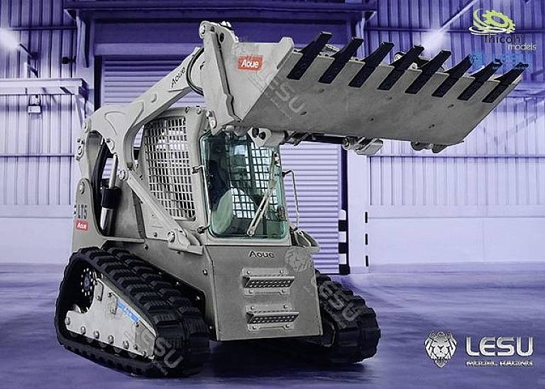 A small, detailed model tracked loader with raised front loader in a warehouse. Doors and graffiti can be seen in the background.