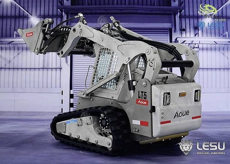 A metallic, chain-driven mini excavator with a bucket arm is positioned in an industrial environment.
