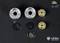 'Four model wheel rims made of metal and plastic in silver, black and gold, with screws, shown against a black background.'