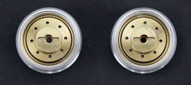 Two round, gold-coloured metal objects with a central hole each, surrounded by small holes, set against a black background.
