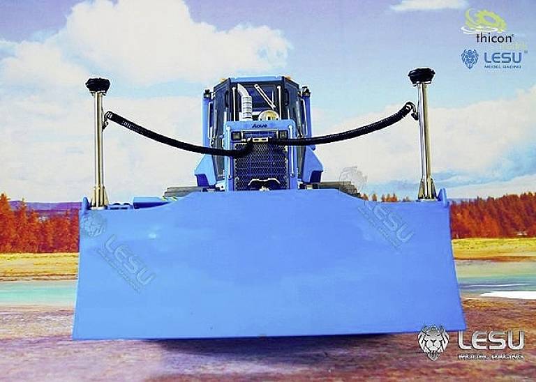 A blue model bulldozer with its bucket raised stands in front of a landscape with trees and sky. Brand logos are visible.