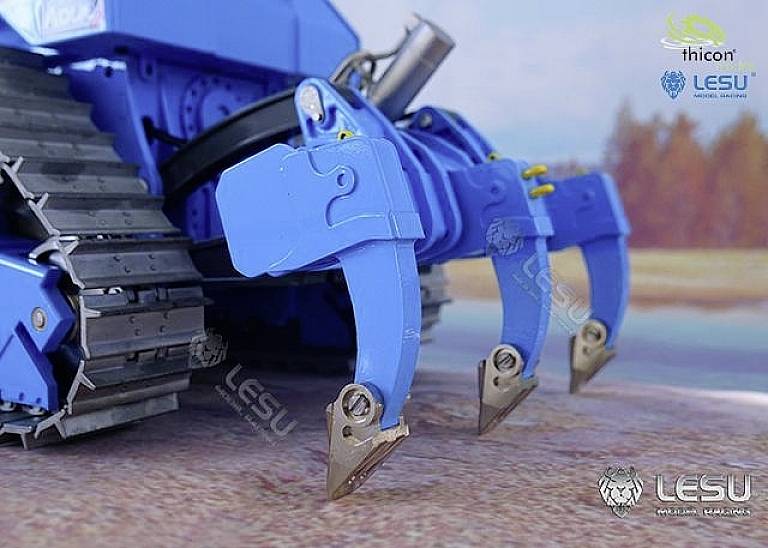 Blue excavator with three robust prongs at the front, suitable for tough digging work. Slightly blurred landscape in the background.