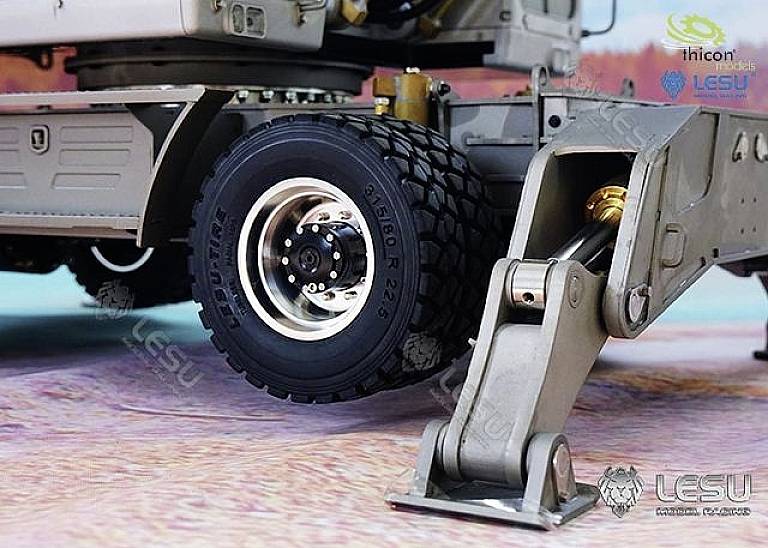 Close-up of a model lorry shows a robust tyre and a boom arm standing on a textured surface.
