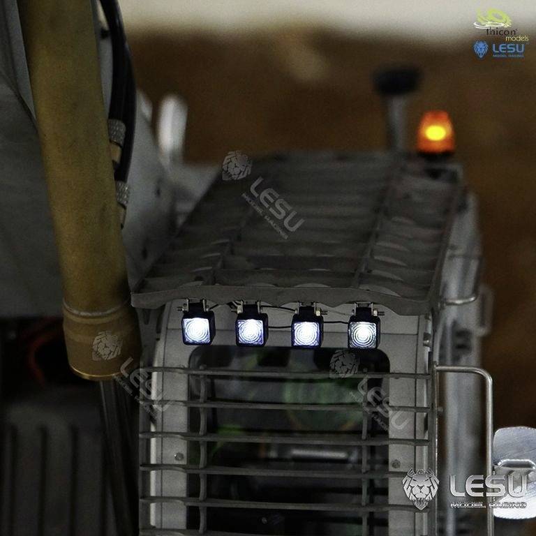 Close-up of a toy construction vehicle with illuminated headlights and an orange warning light. Background blurred.