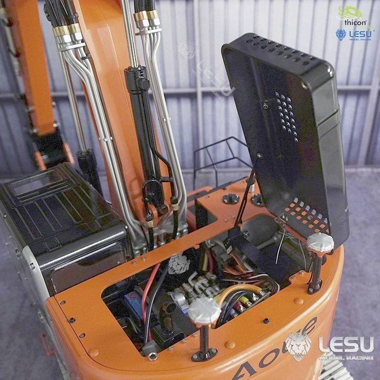 An orange excavator with its bonnet open reveals exposed cables and components, standing in a storage room.
