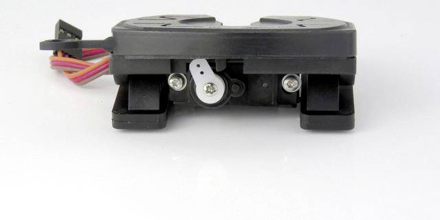 A black, rectangular electronic device with connected cables is lying on a white surface.