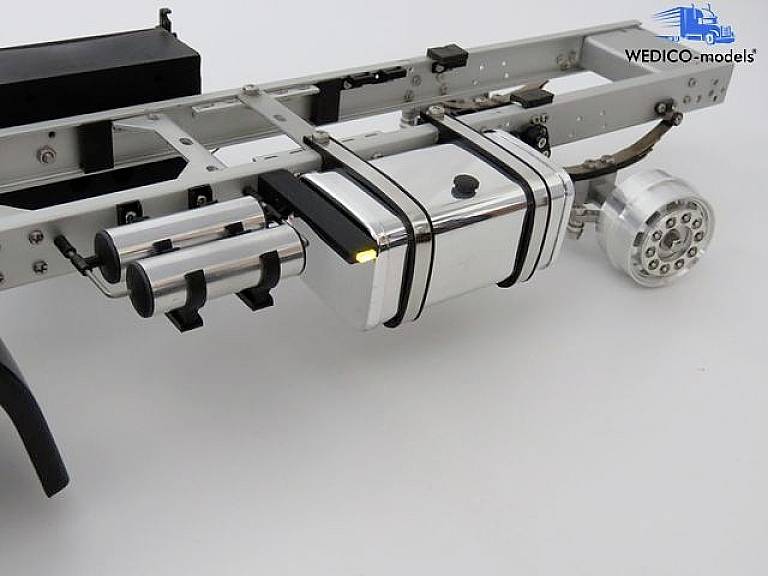 Lorry model chassis with exhaust pipes and WEDICO logo. Silver-coloured fuel tank, black details, focus on technical elements.