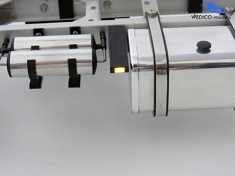 A silver device on a white background with a black logo in the top right corner. Two cylindrical elements on the left, a rectangular module on the right.