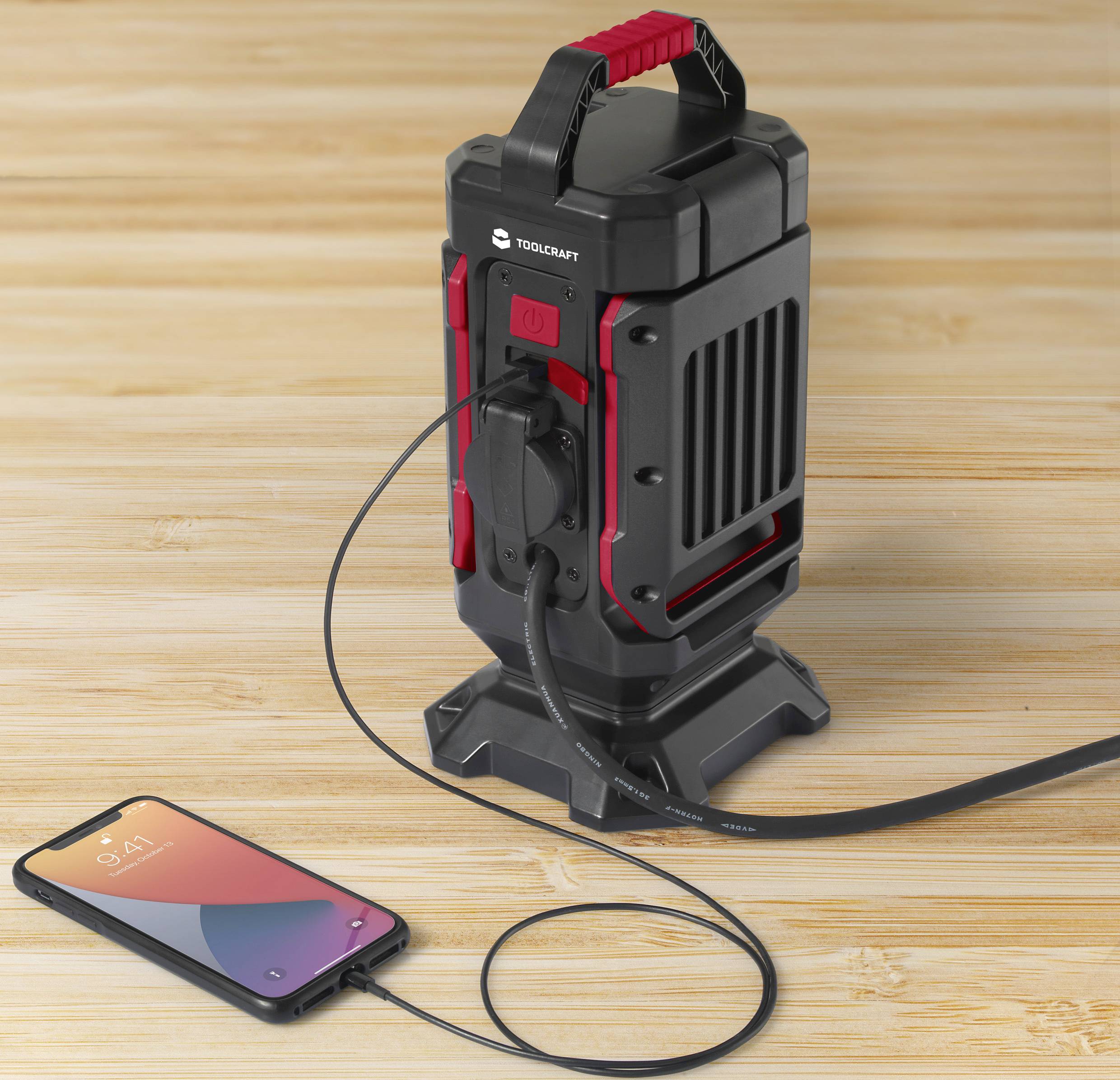 A portable charging tower charges a smartphone via a cable resting on a wooden table.