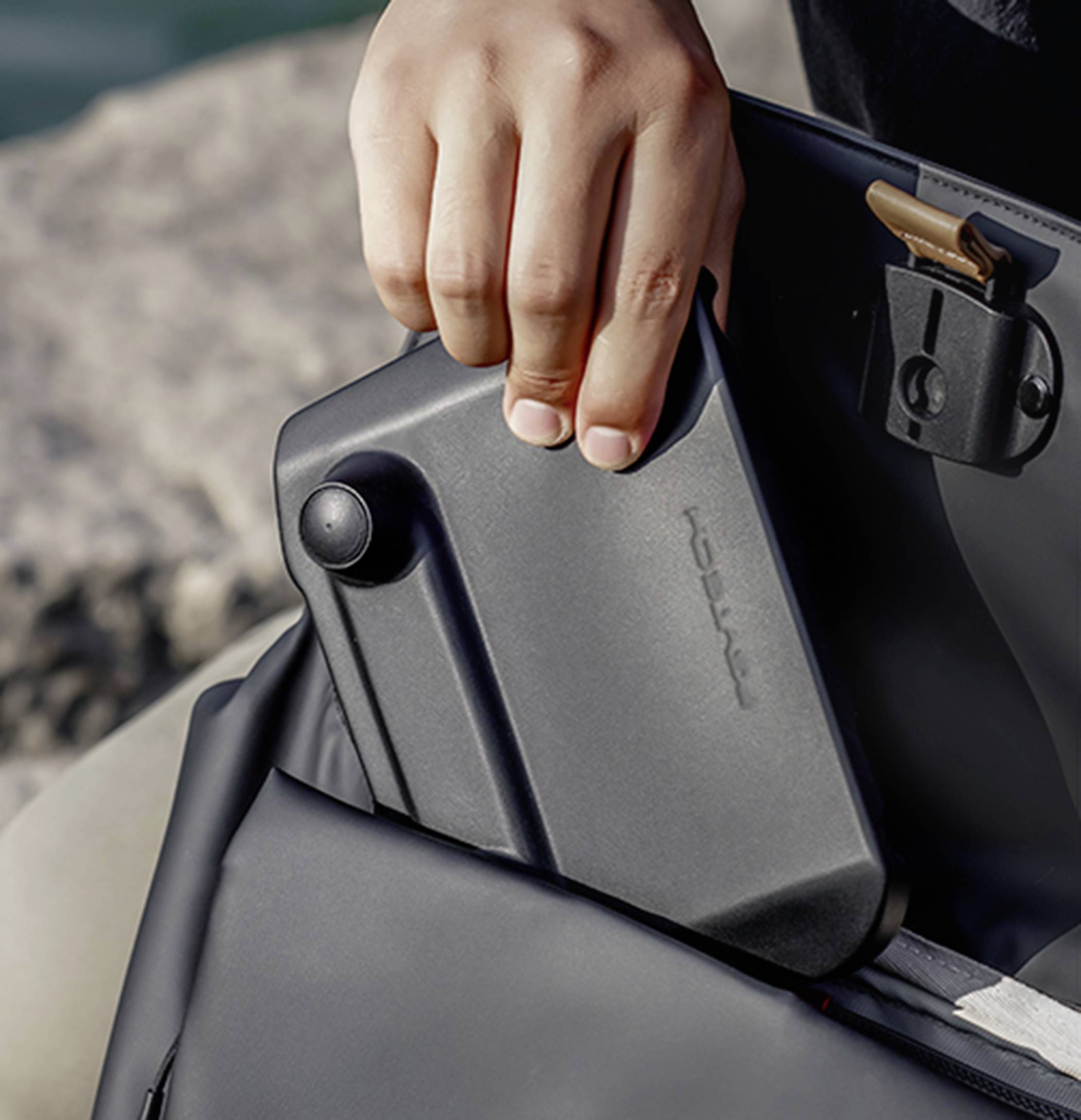 A hand takes a black device with a small lever out of a bag. It looks like a portable electronic device.