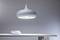A modern, white pendant light illuminates a white table with two white bowls, set against a minimalist grey background.