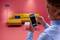A man looks at his mobile phone while standing in front of a yellow sofa in a pink room. The phone displays a tick symbol.