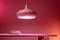 A pink lamp hangs over a table with two white bowls. The light creates a warm, atmospheric ambience in the room.