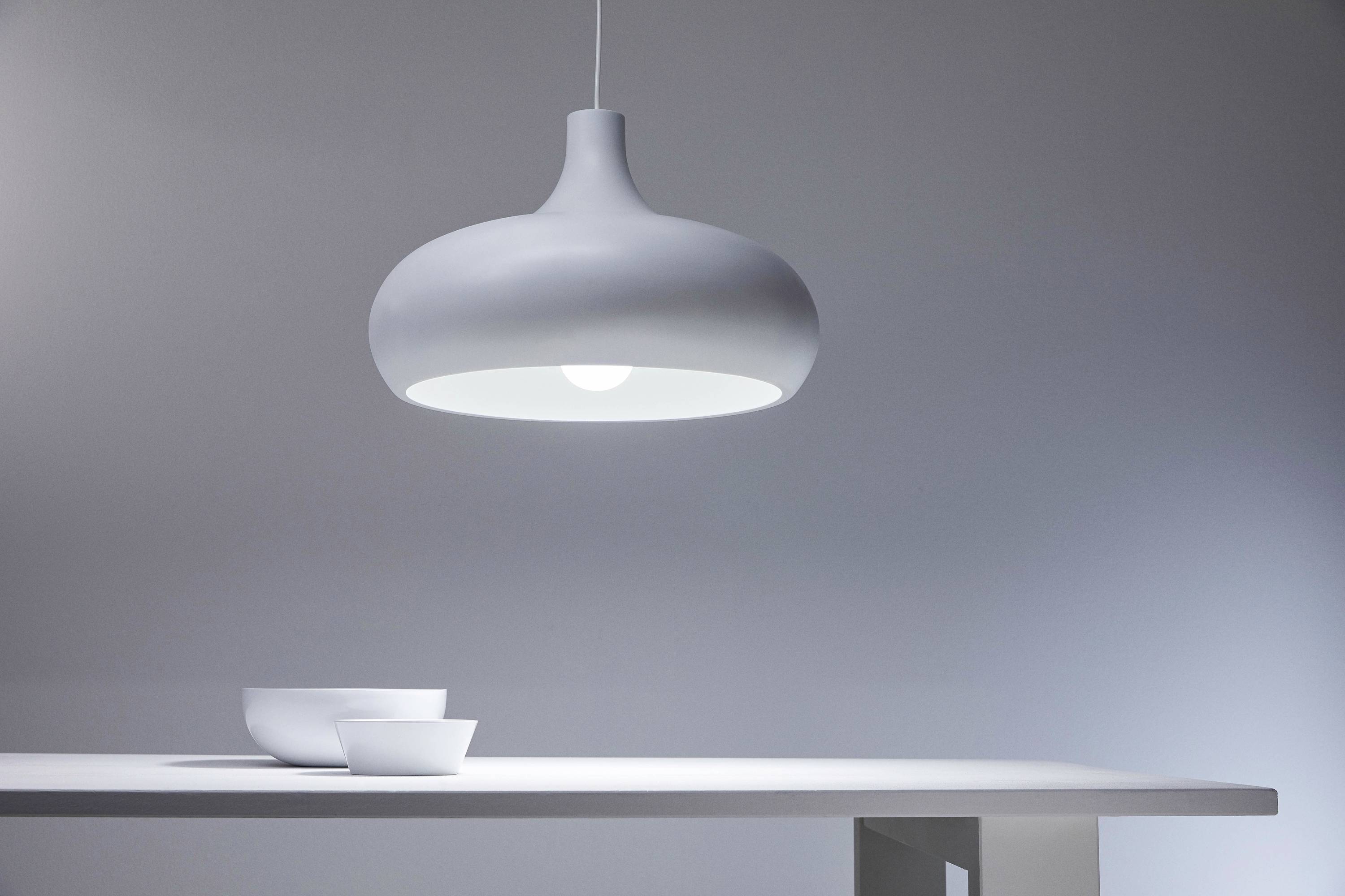 A simple white pendant light illuminates a table with two white bowls. The scene conveys modernity and minimalism.