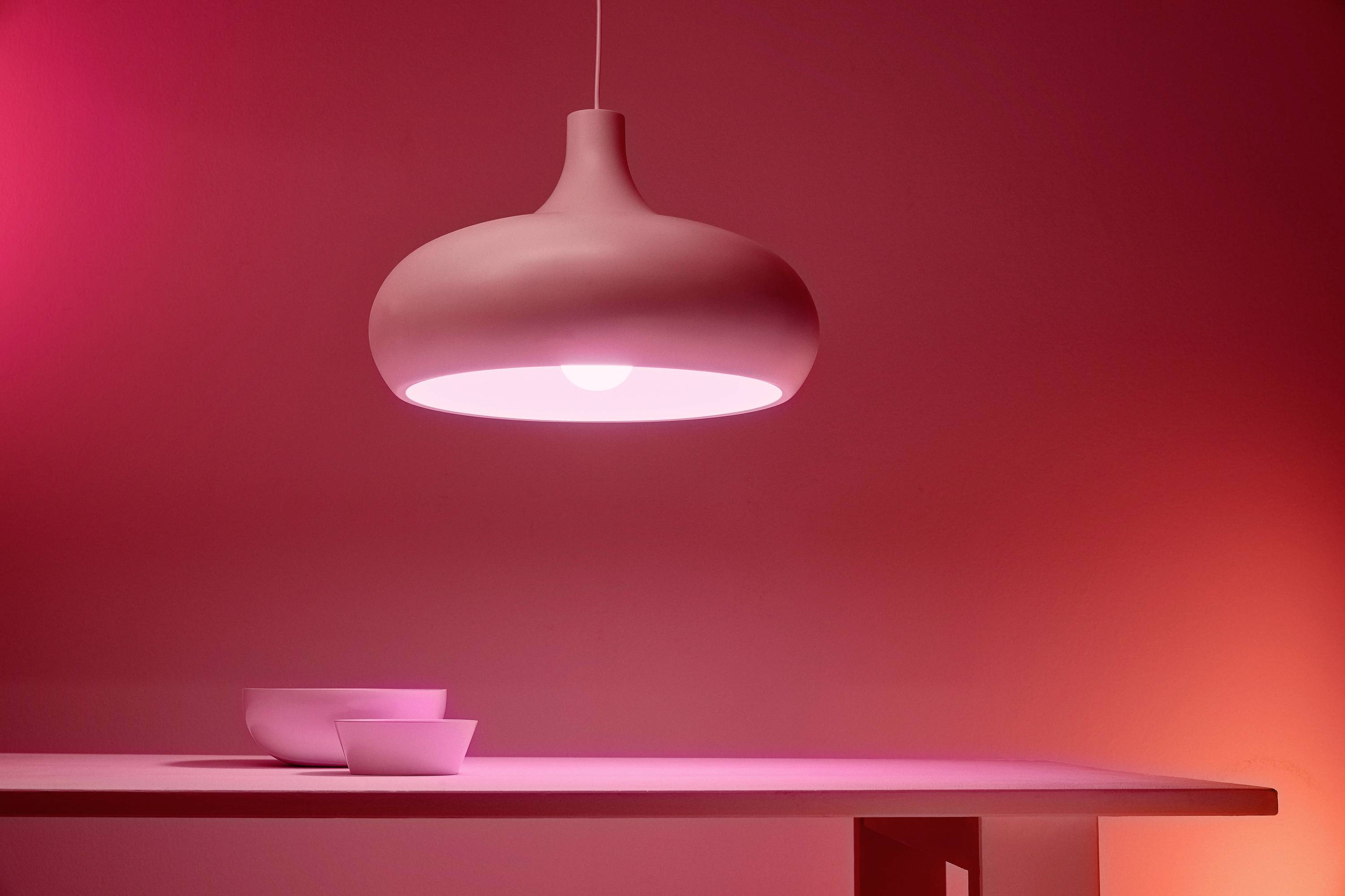 A contemporary, pink-glowing pendant light hanging over a table with two white bowls, illuminated in a moody red light.