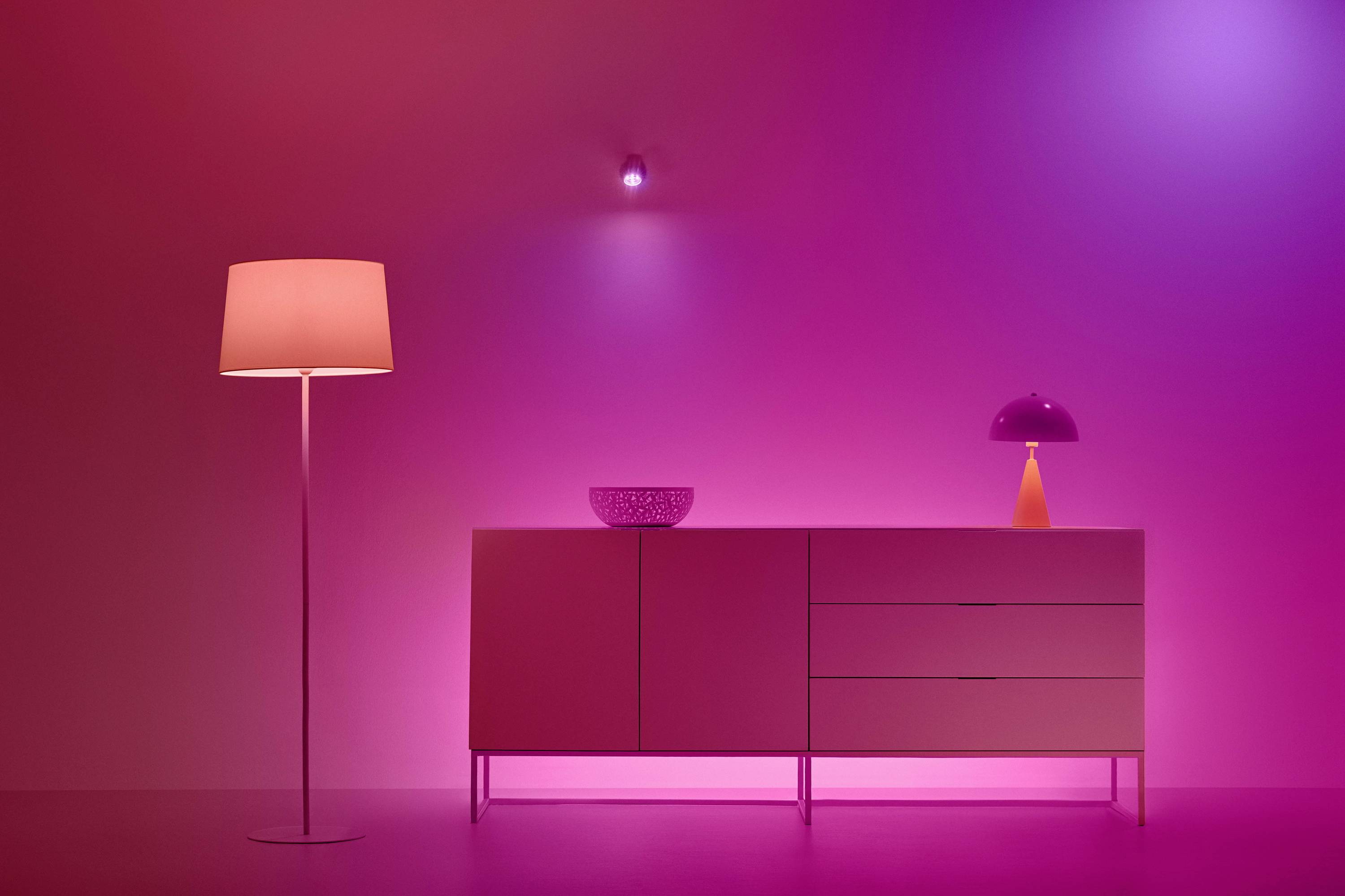 A contemporary room with a pink glowing standard lamp, sideboard, and table lamp. The space is illuminated in warm pink and purple hues.