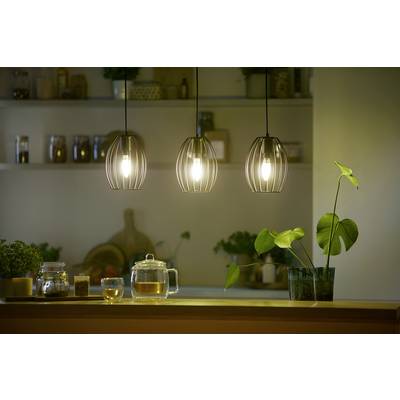 Three pendant lights illuminate a kitchen counter with a teapot, cup, and plant. In the background, shelves with spice jars are visible.