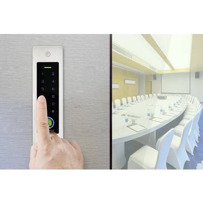 A hand presses a button on a black touchpad next to a conference room with an oval table and white chairs.