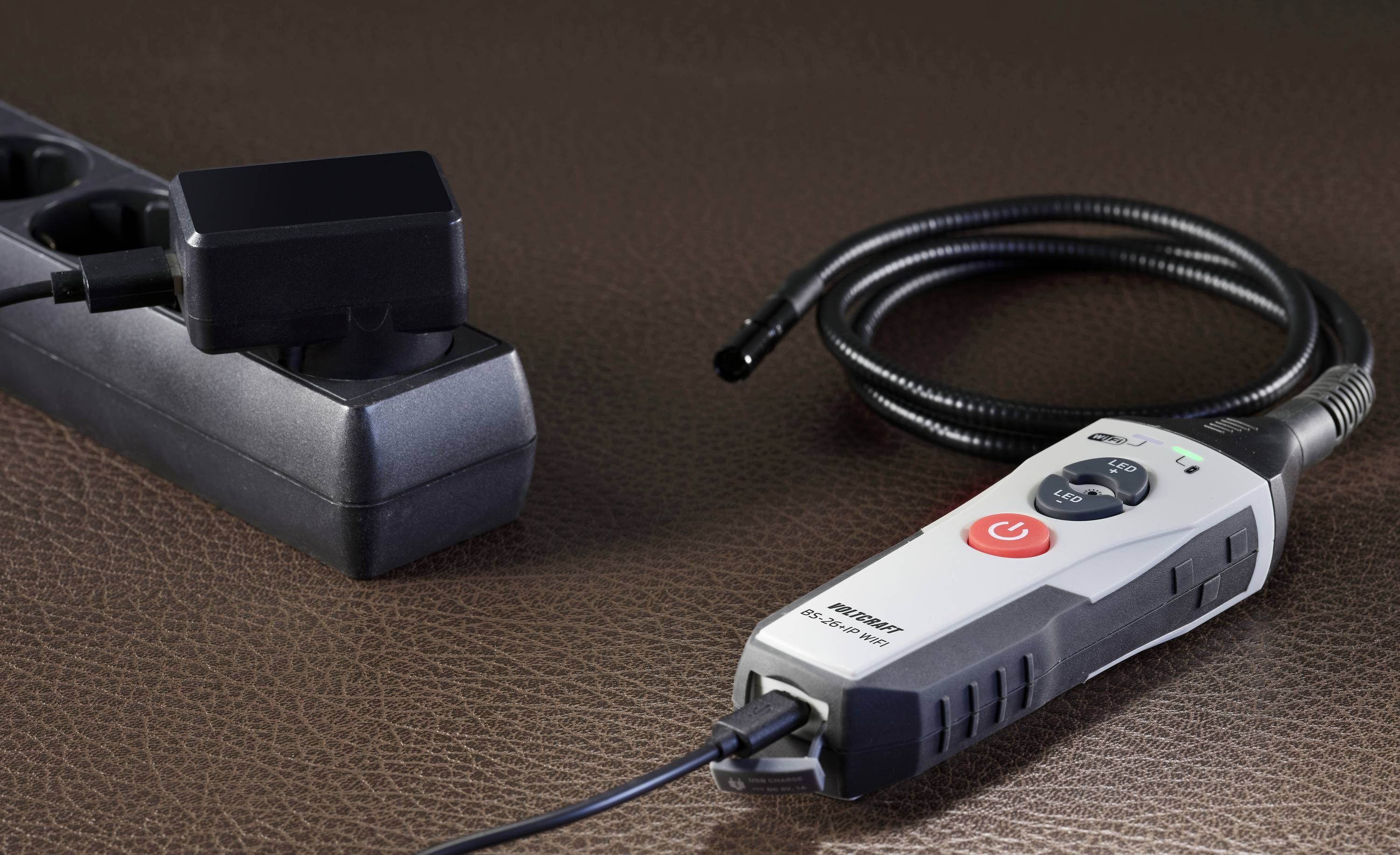 A multi-socket extension lead and an electric tool with a red switch are lying on a brown surface.