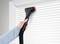 A person is cleaning white venetian blinds with a brush attachment on a vacuum cleaner.