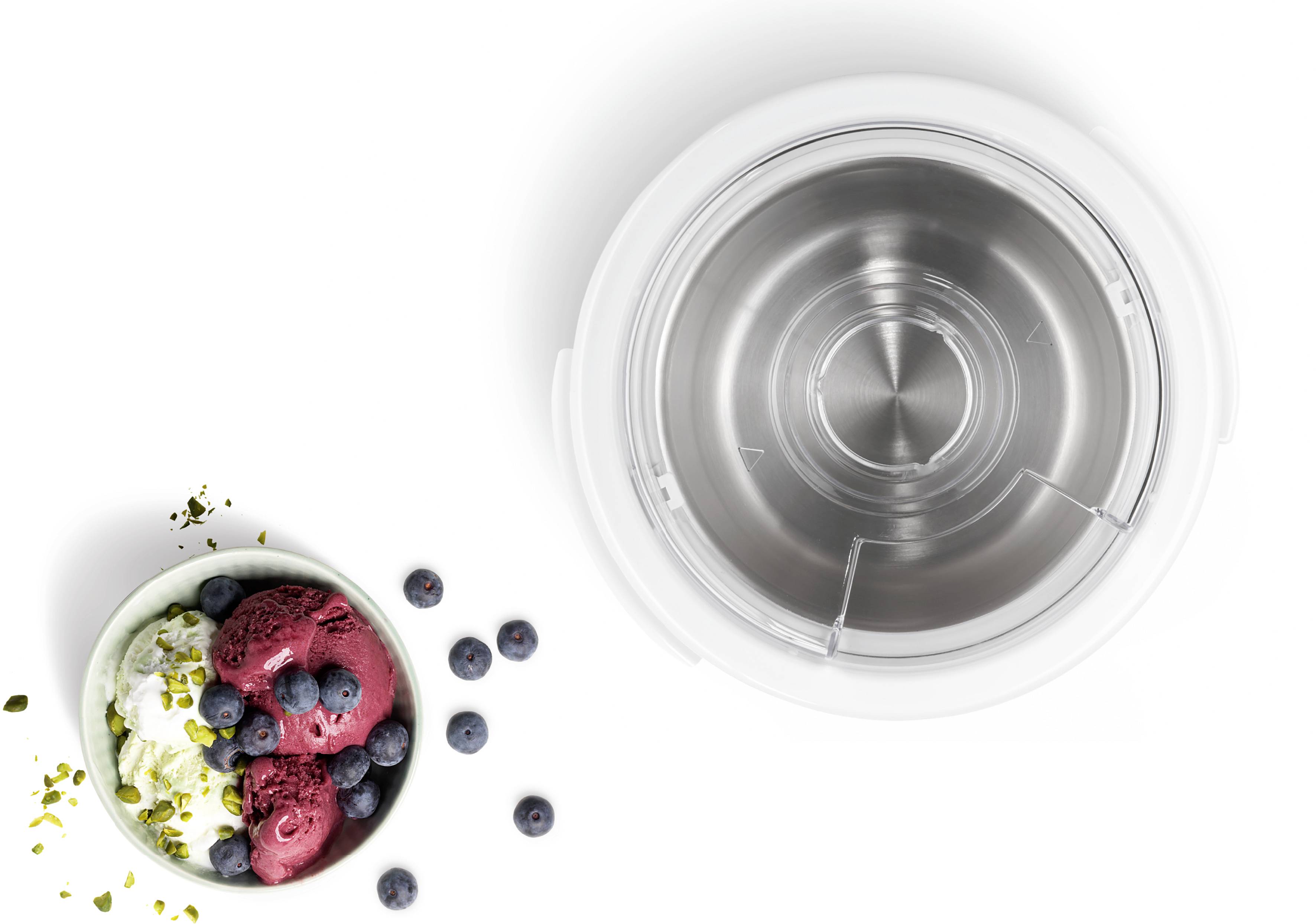 A bowl of ice cream, garnished with blueberries and pistachios, beside an empty, gleaming metal bowl.