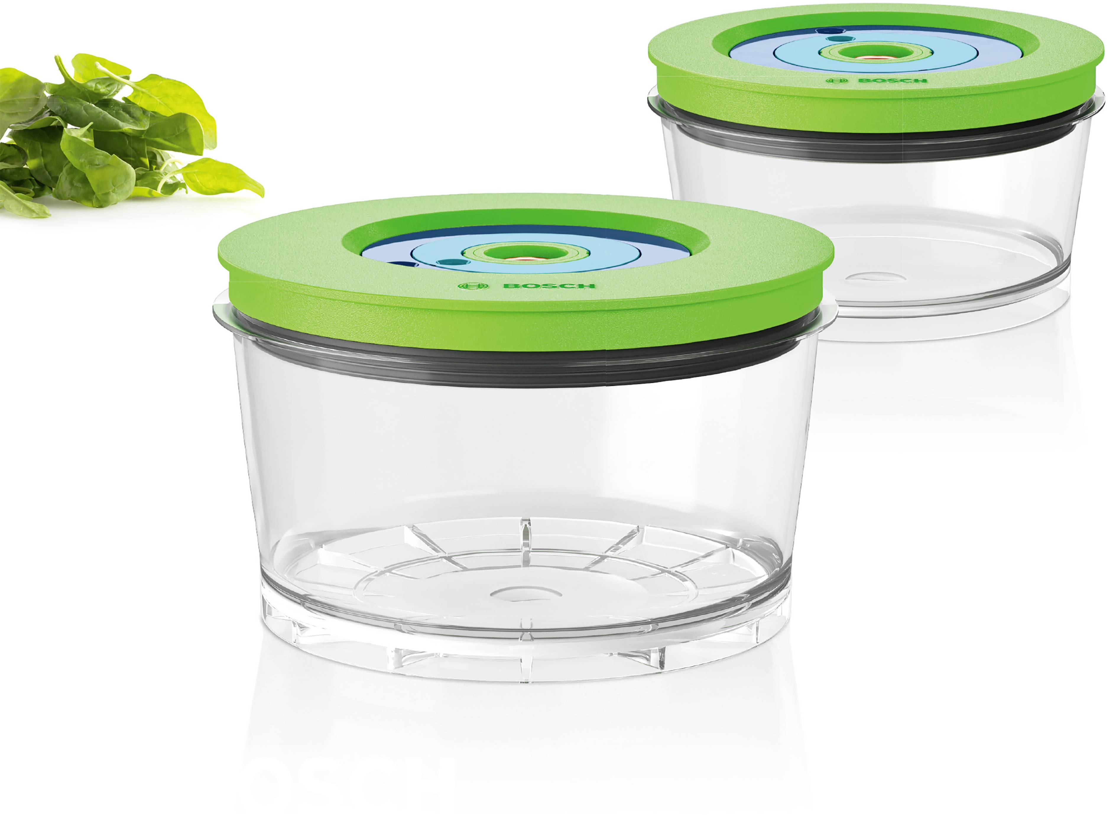 Two transparent, round food storage containers with green lids next to fresh spinach. Containers by Bosch, suitable for storage.
