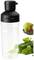 A transparent mixer container with a black lid, next to a halved avocado and fresh spinach leaves.