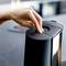 A hand presses the lid of a black electric kitchen waste bin. Background blurred.