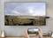 A person is streaming a nature photo featuring a rainbow, rocks, and clouds from a smartphone to a television mounted on the wall.