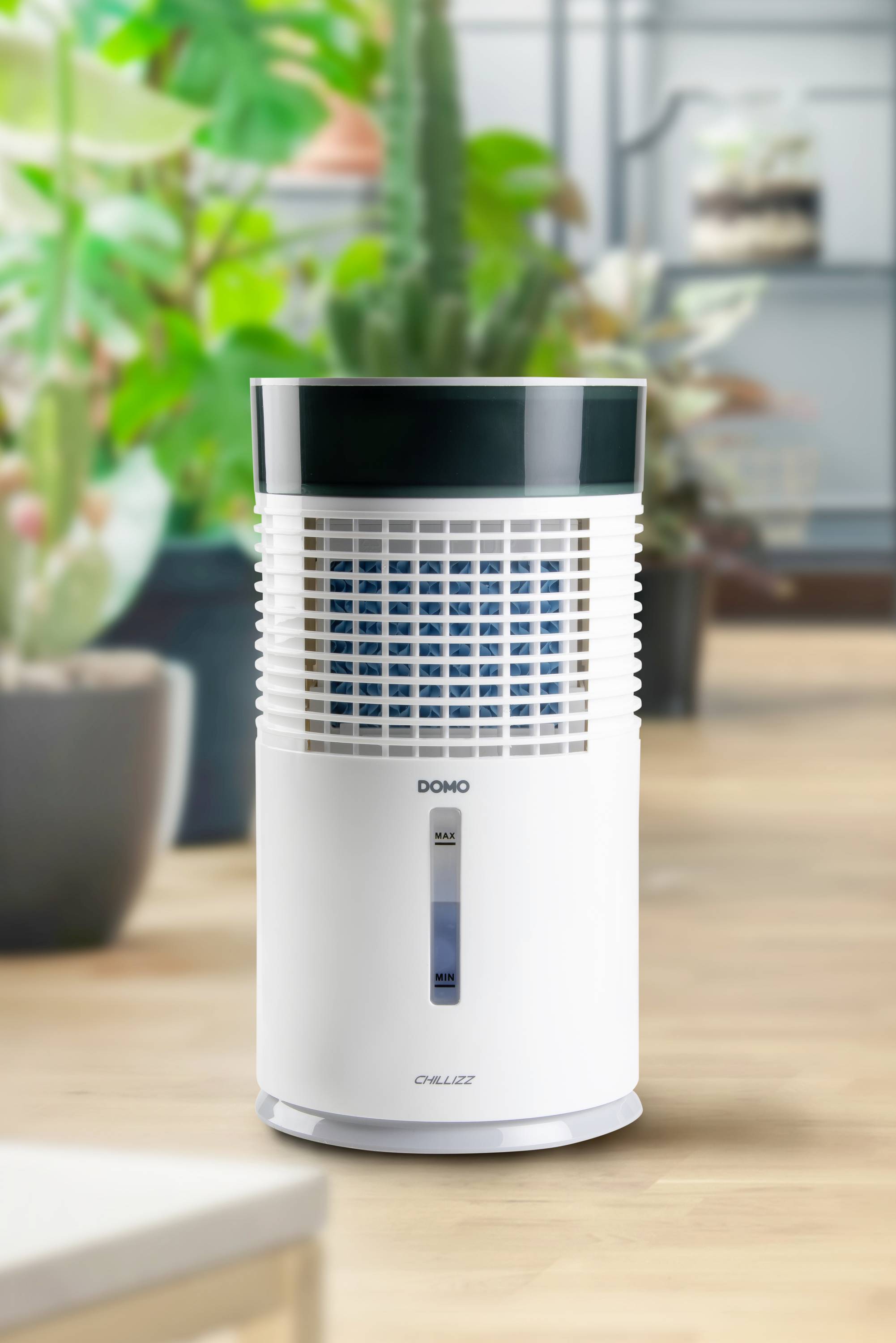 A compact dehumidifier stands on a wooden floor, surrounded by green plants, in a modern, bright room.
